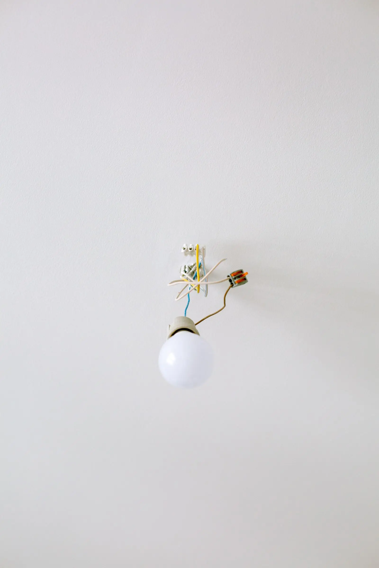Light bulb hanging from exposed wires and connectors on a white ceiling