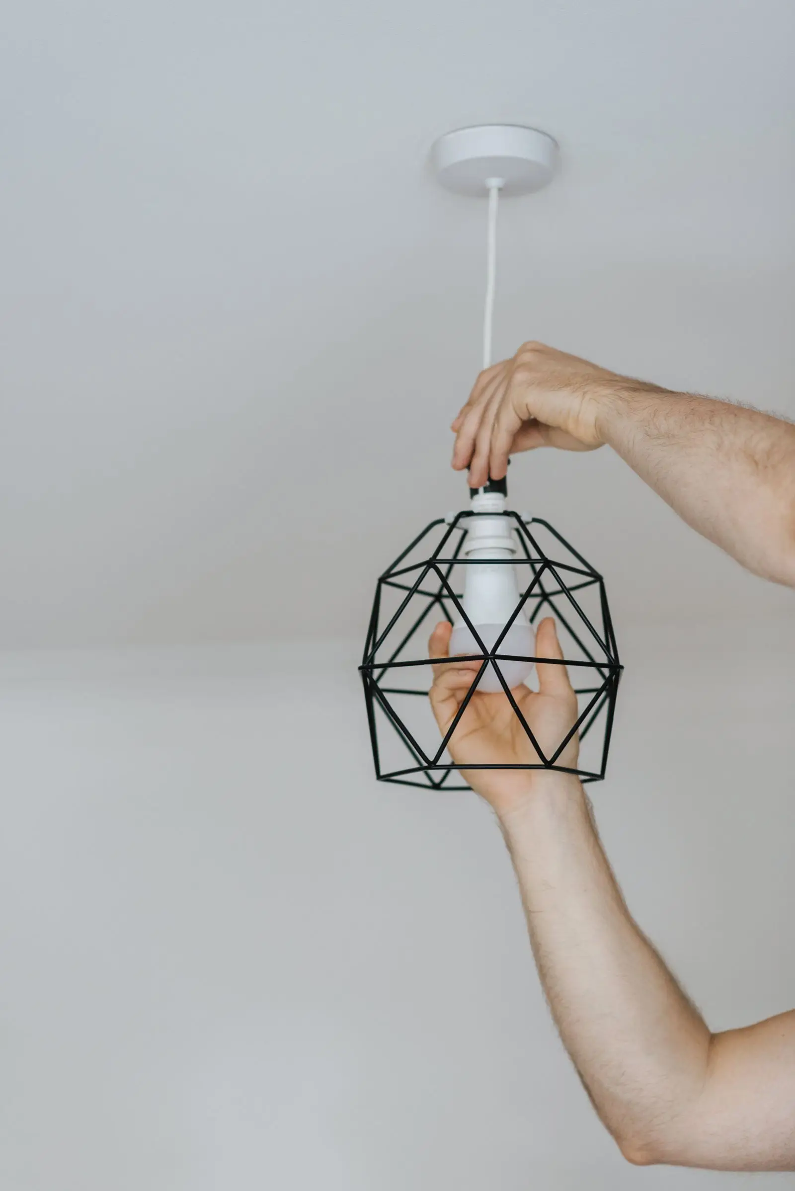 Hands screwing a bulb into a wire-cage pendant fixture