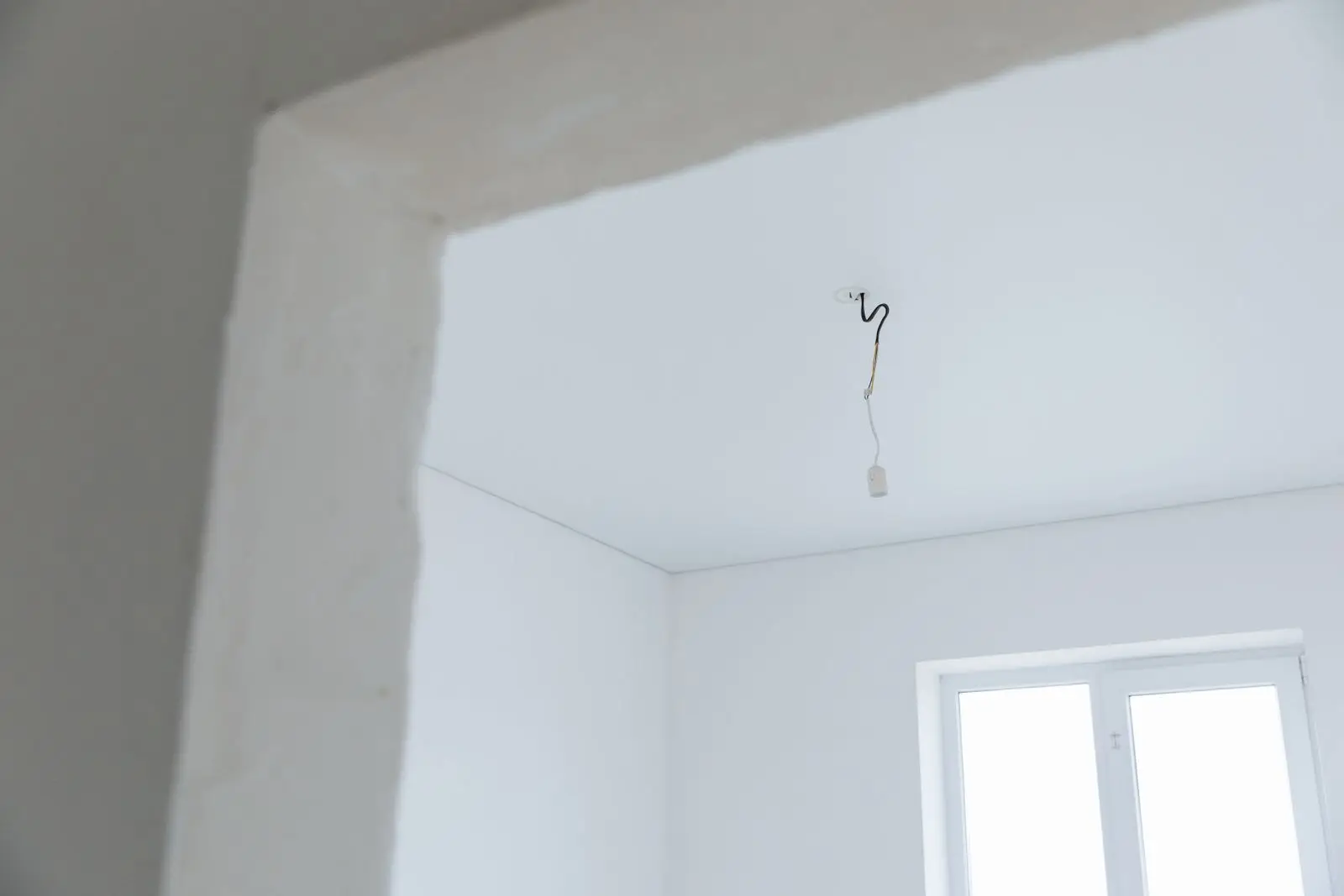 Single wire hanging from the ceiling of a freshly plastered empty room