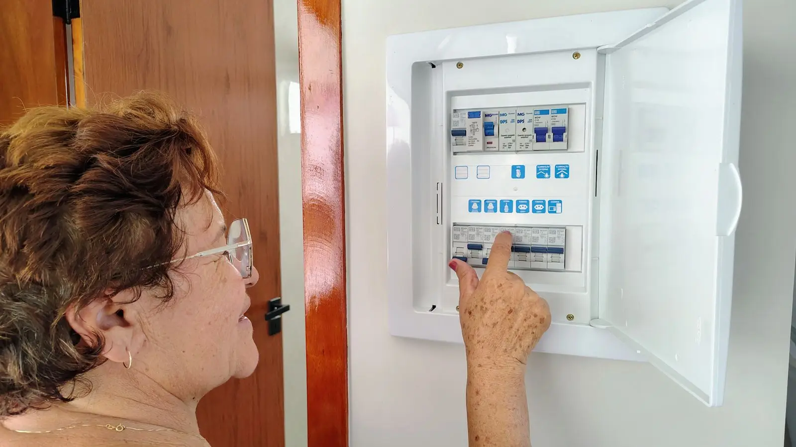 Older woman pointing at a breaker inside a wall-mounted distribution box