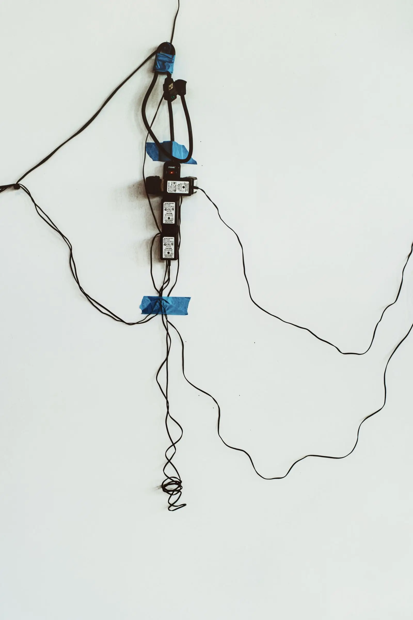Outlet held to a wall with tape, with thin cords trailing across the wall