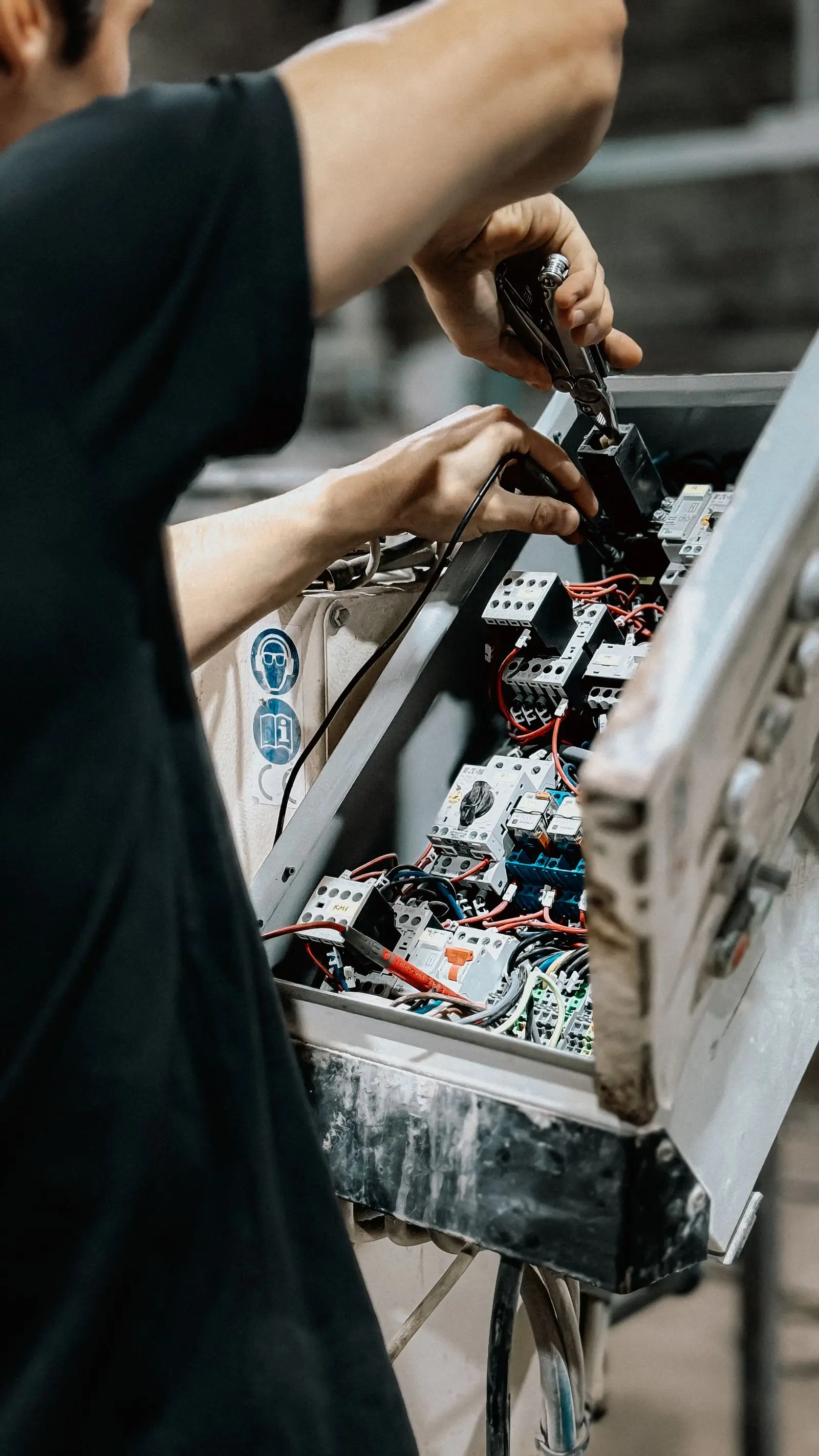 Technician reaching into a control panel filled with contactors and wiring