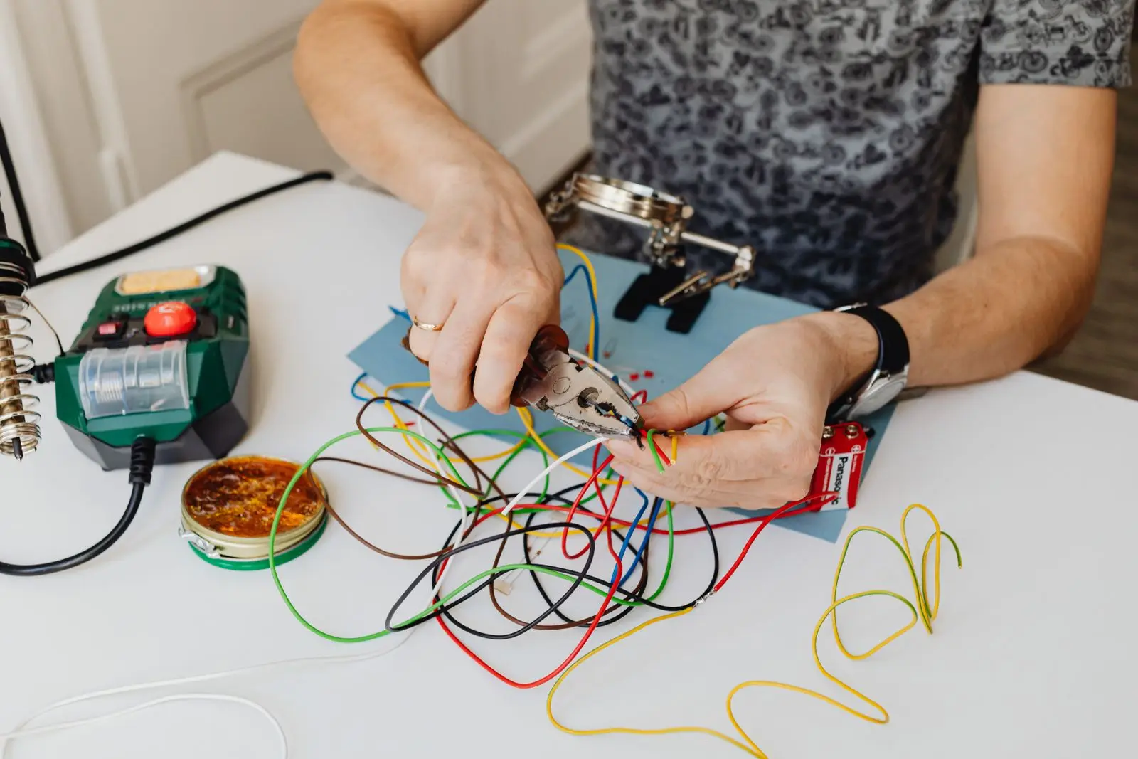 Hands cutting insulated wire with pliers at a work table covered in coloured wire