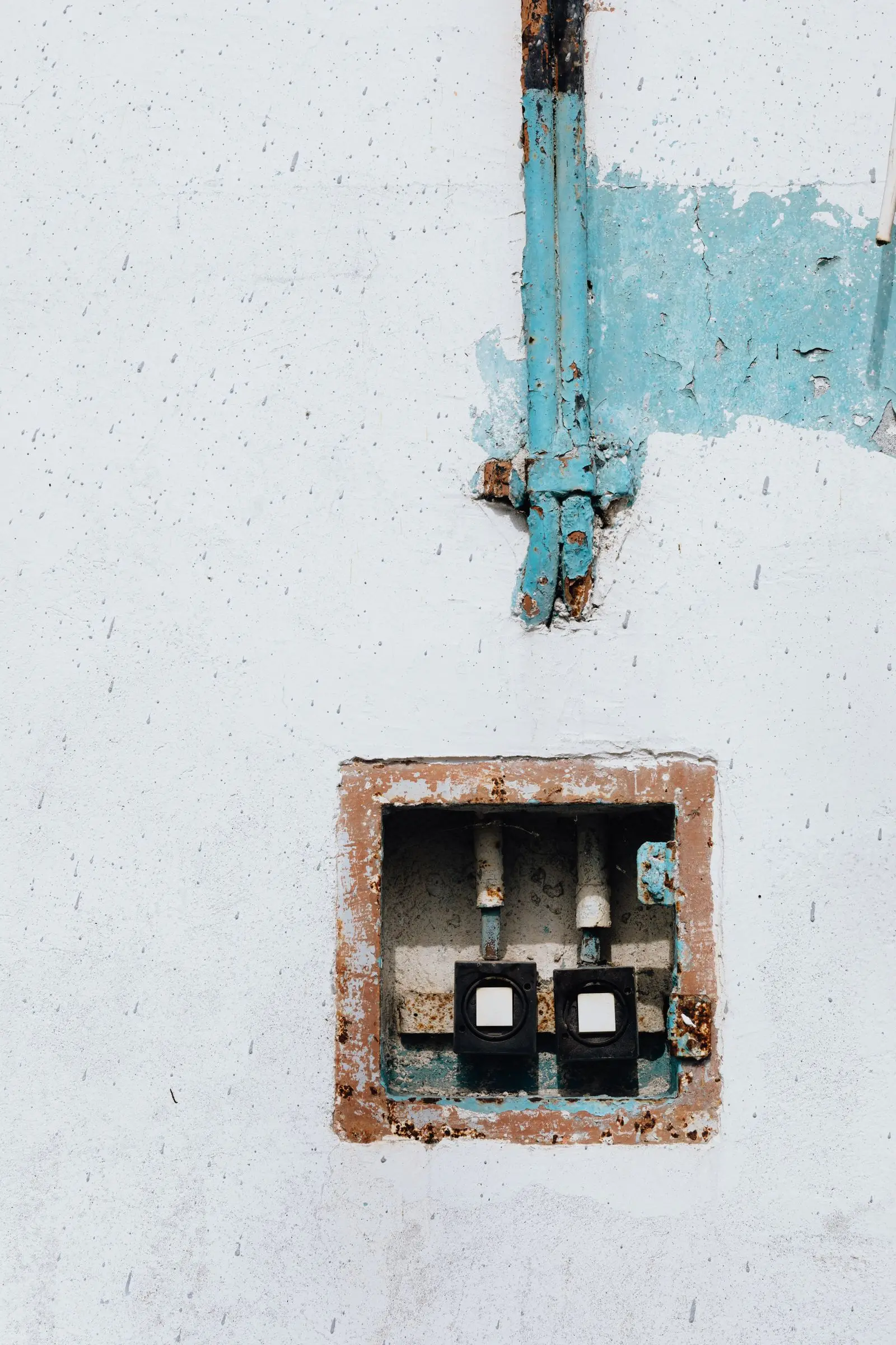 Open wall box with exposed terminals in a wall with peeling paint