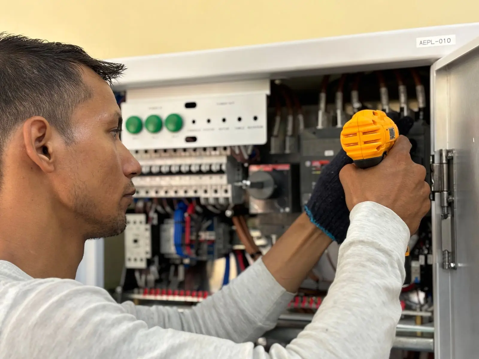 Electrician in work gloves using a cordless driver inside a breaker cabinet