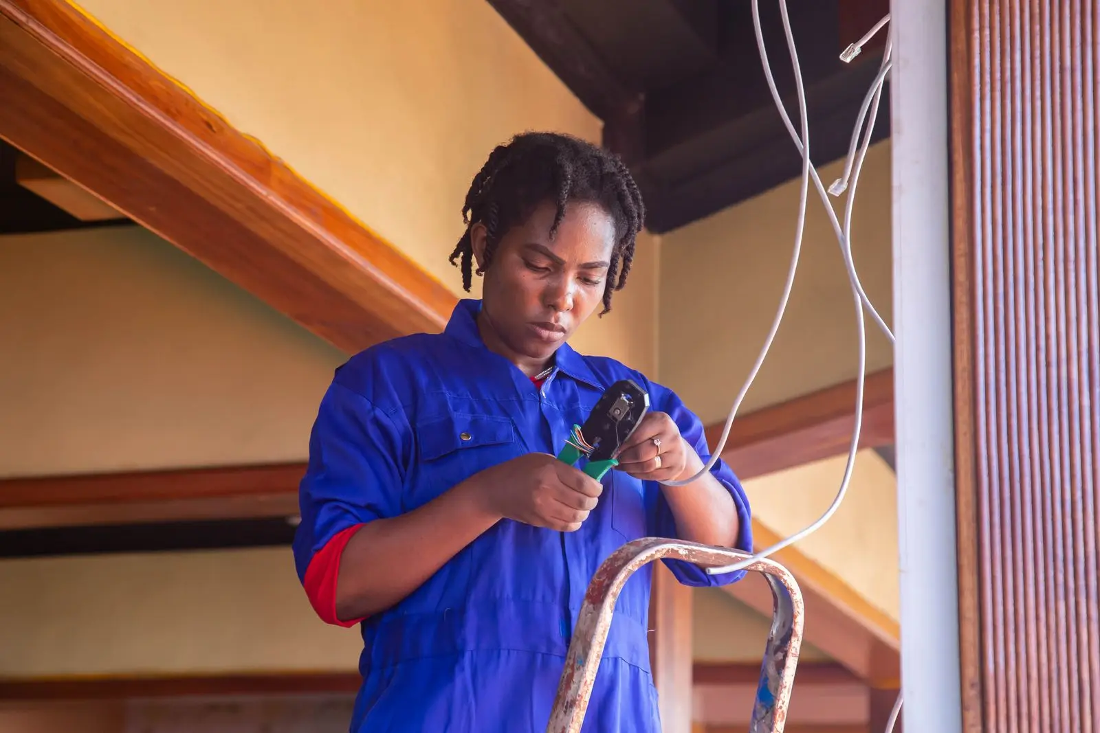 Electrician in blue coveralls preparing a length of cable beside a stepladder