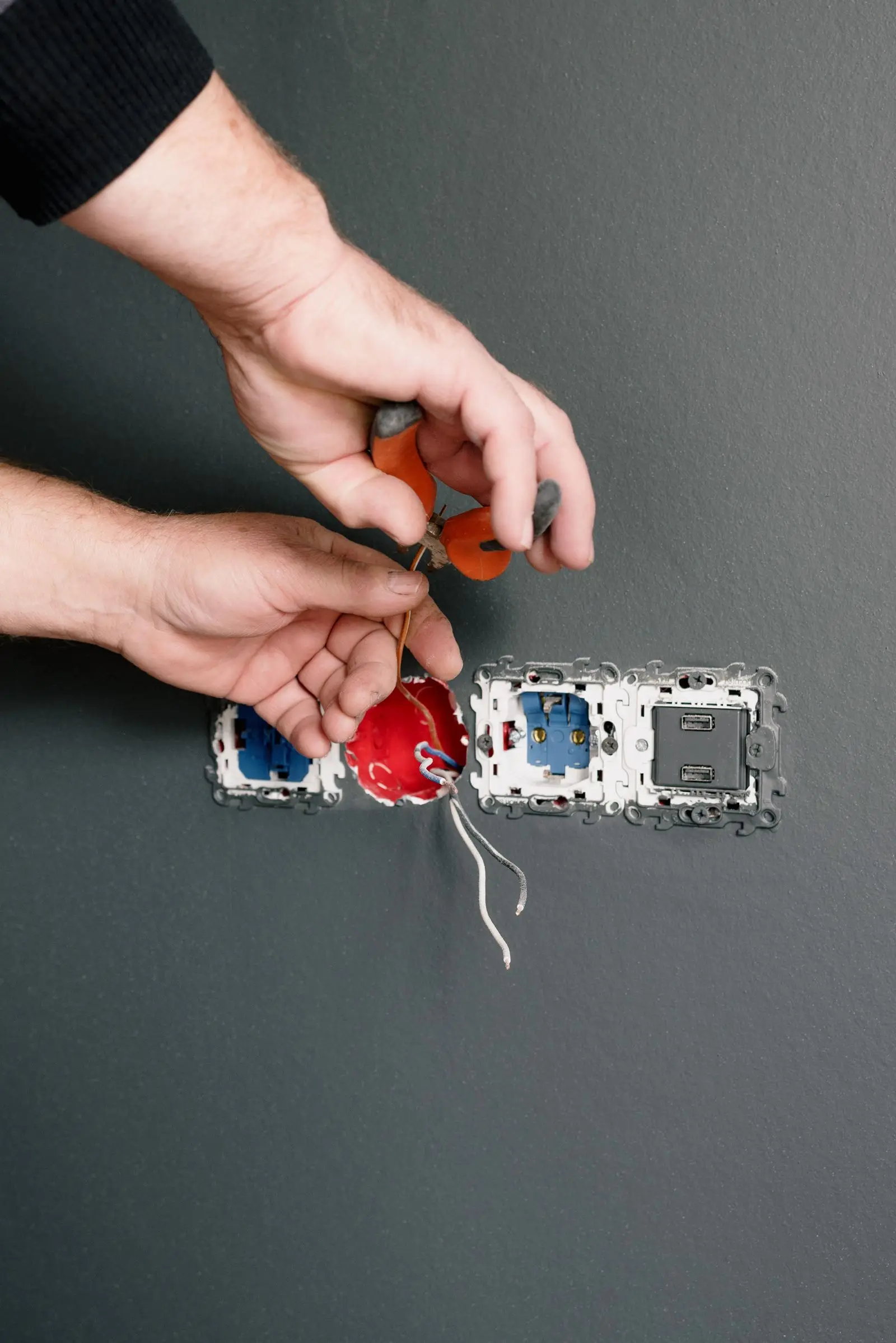 Hands with pliers working on a row of wall boxes during socket installation