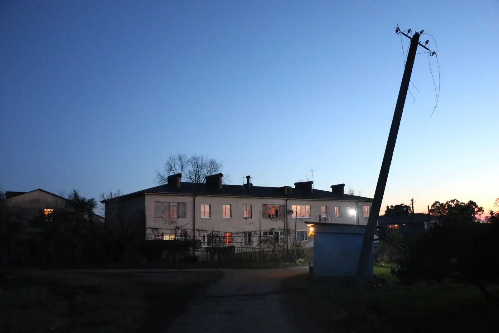 Leaning utility pole beside a lit building at dusk