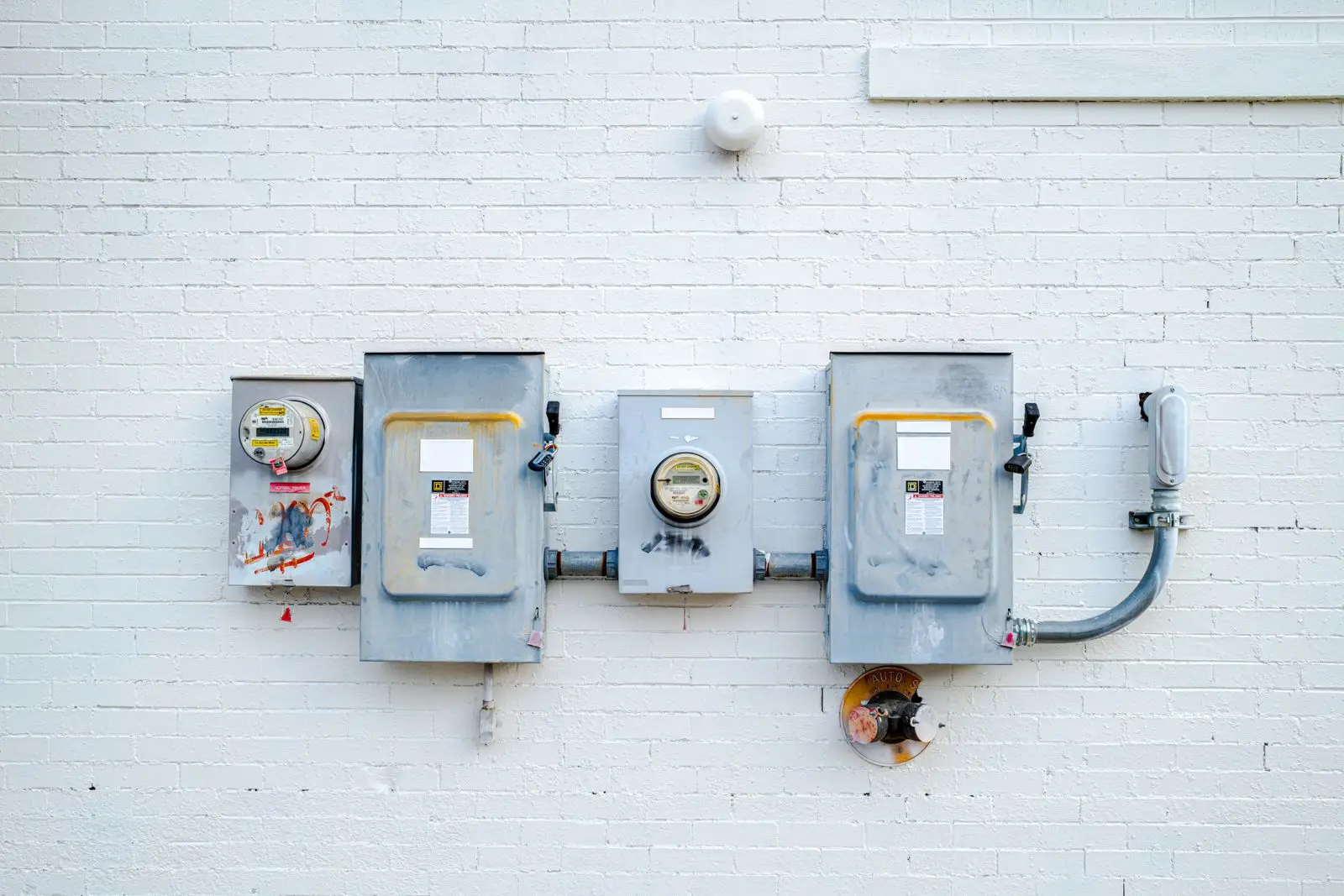 Electric meters and disconnect boxes mounted on a white brick wall