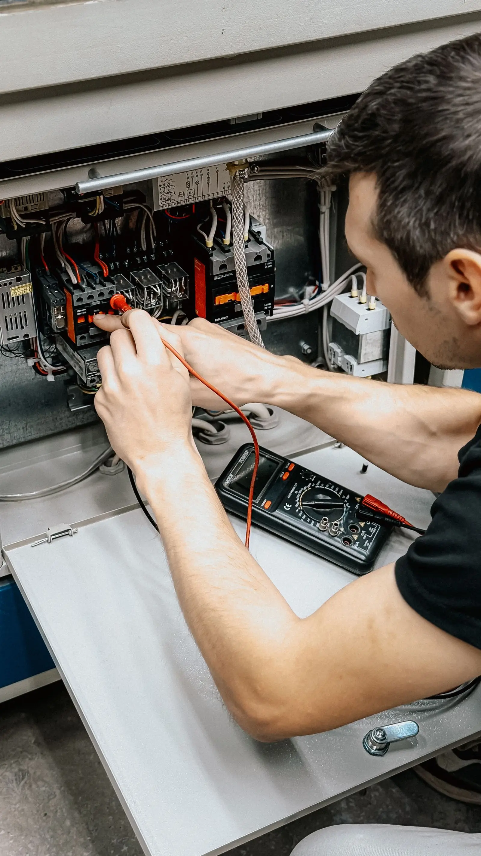 Electrician holding multimeter probes on terminals inside an open electrical cabinet