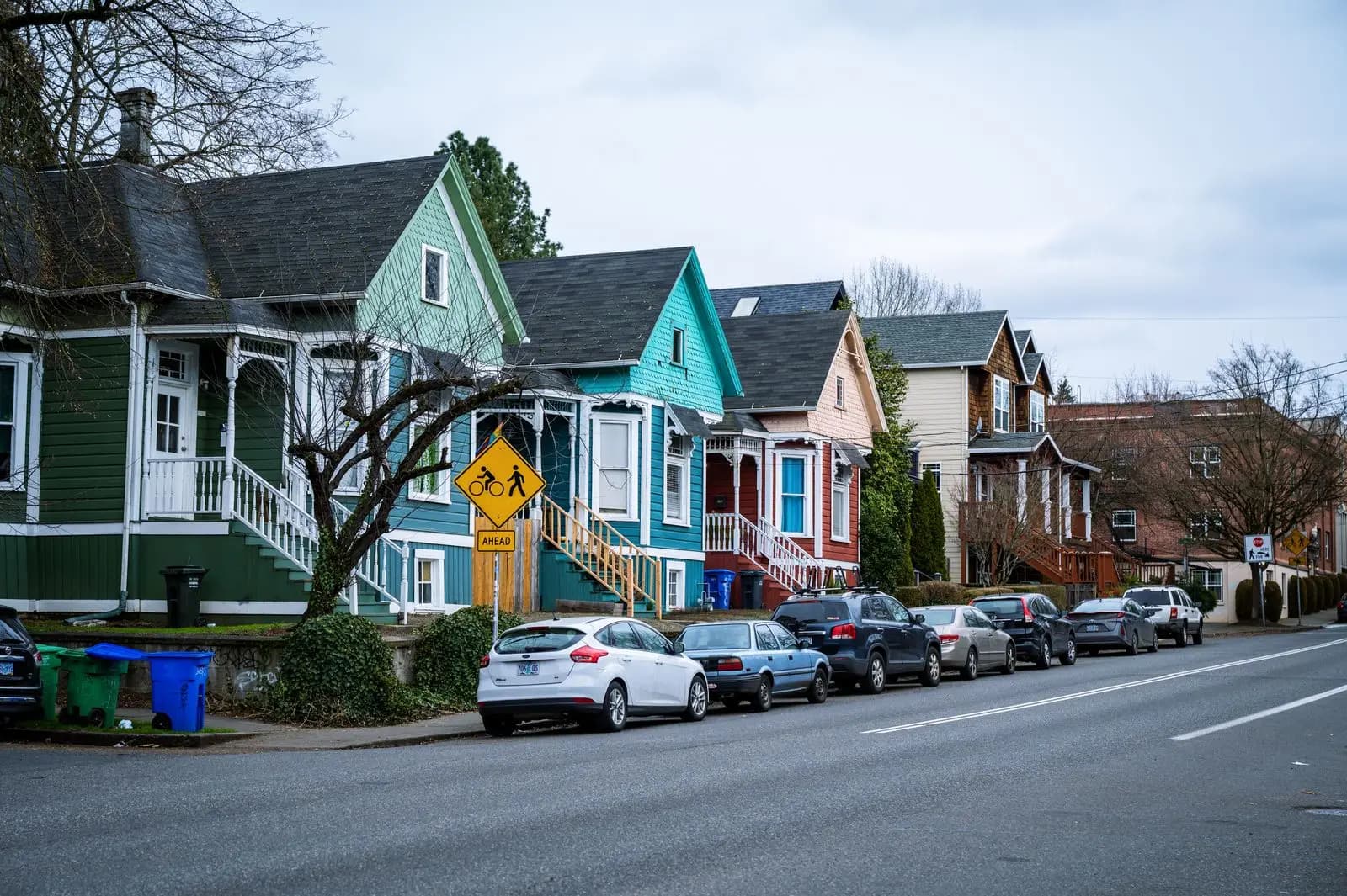 Street of brightly painted older wooden houses with cars parked along the curb