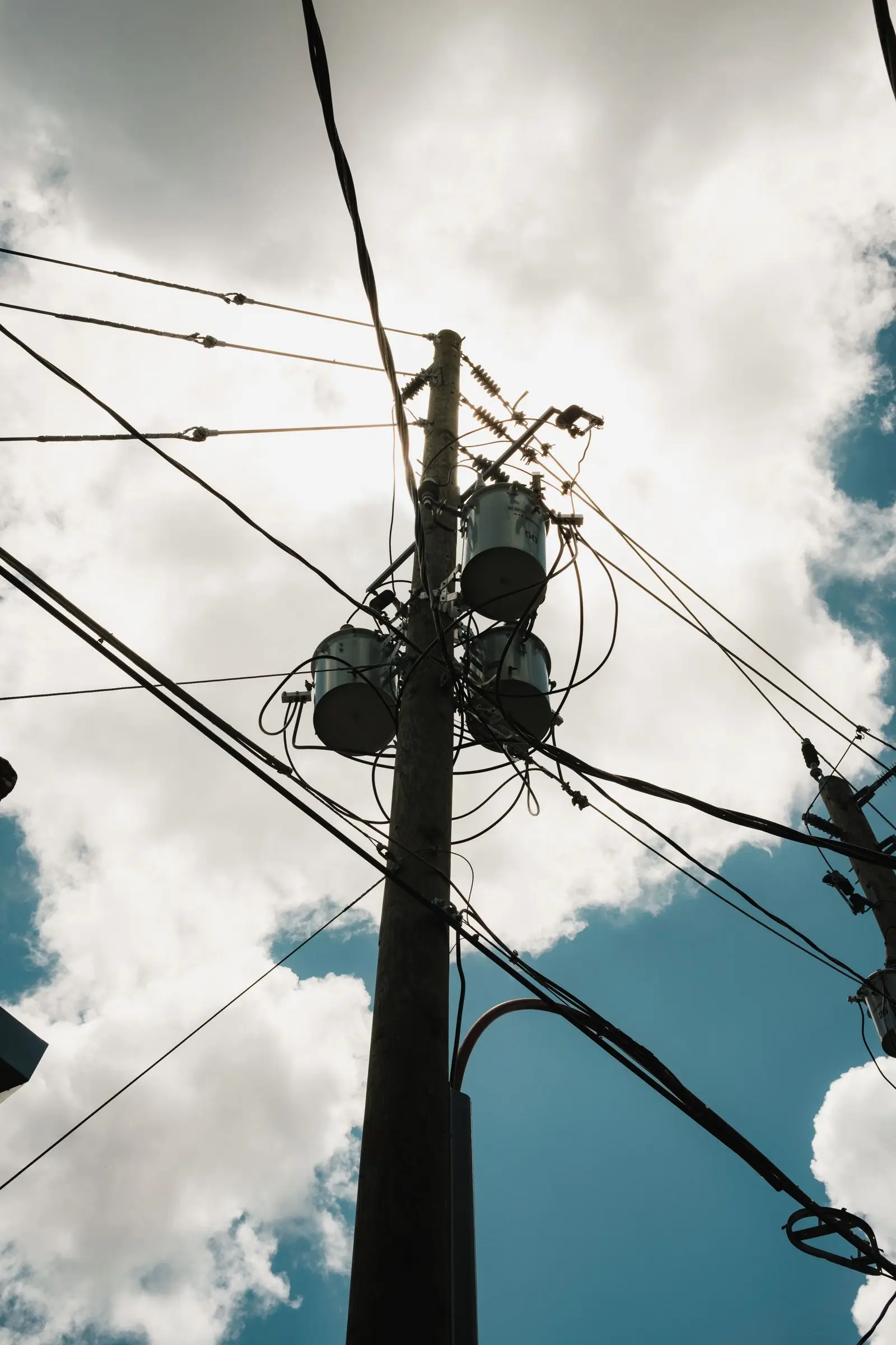 Utility pole carrying three transformers against a cloudy sky