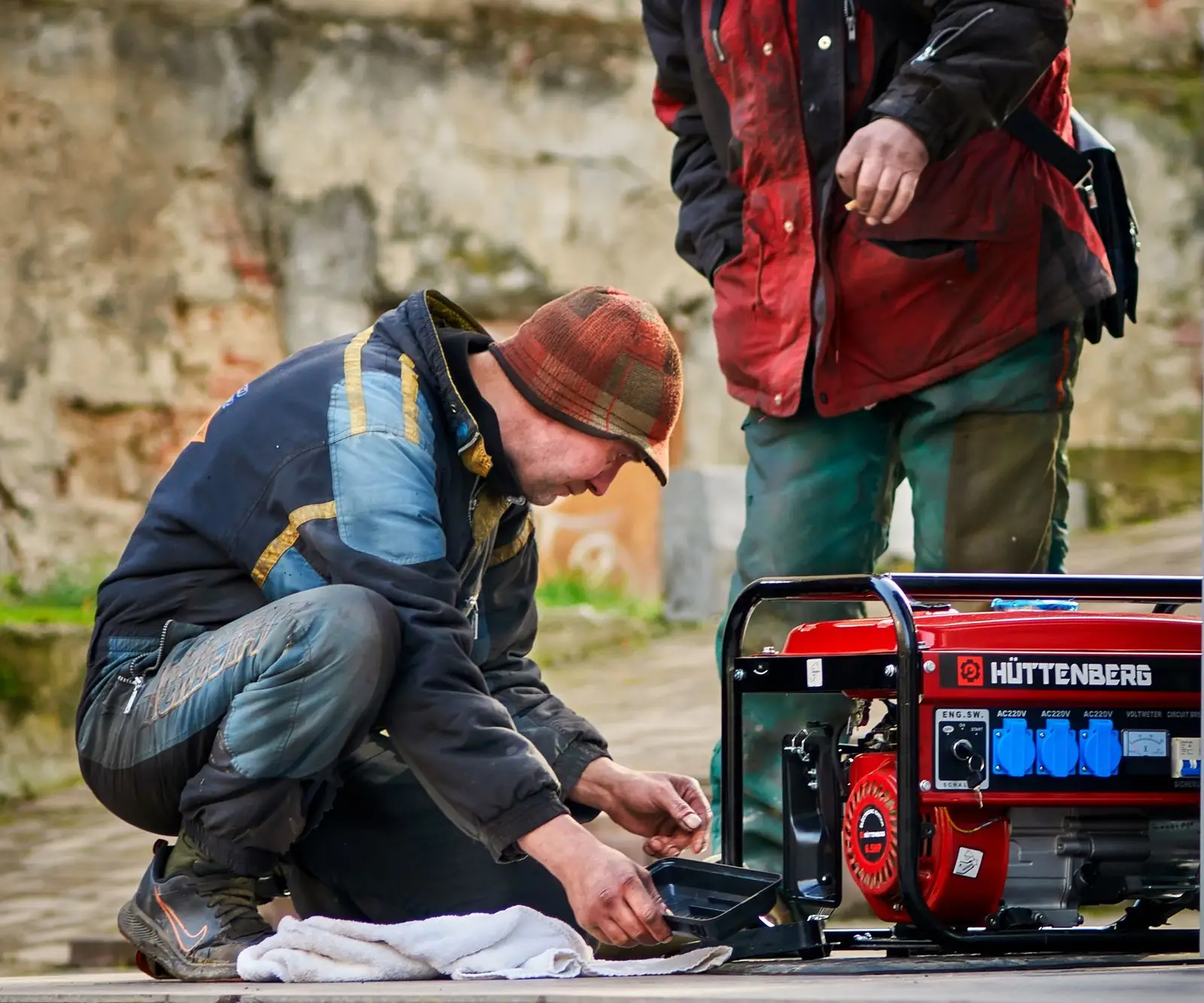 Two people crouched beside a red portable generator outdoors
