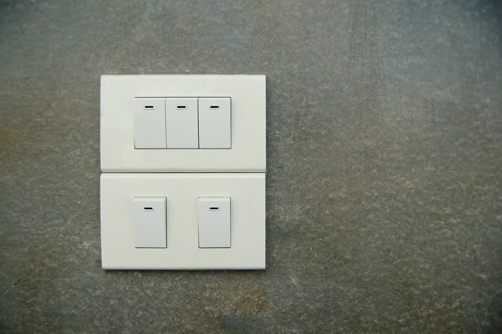 Two plates of white rocker switches on a grey wall