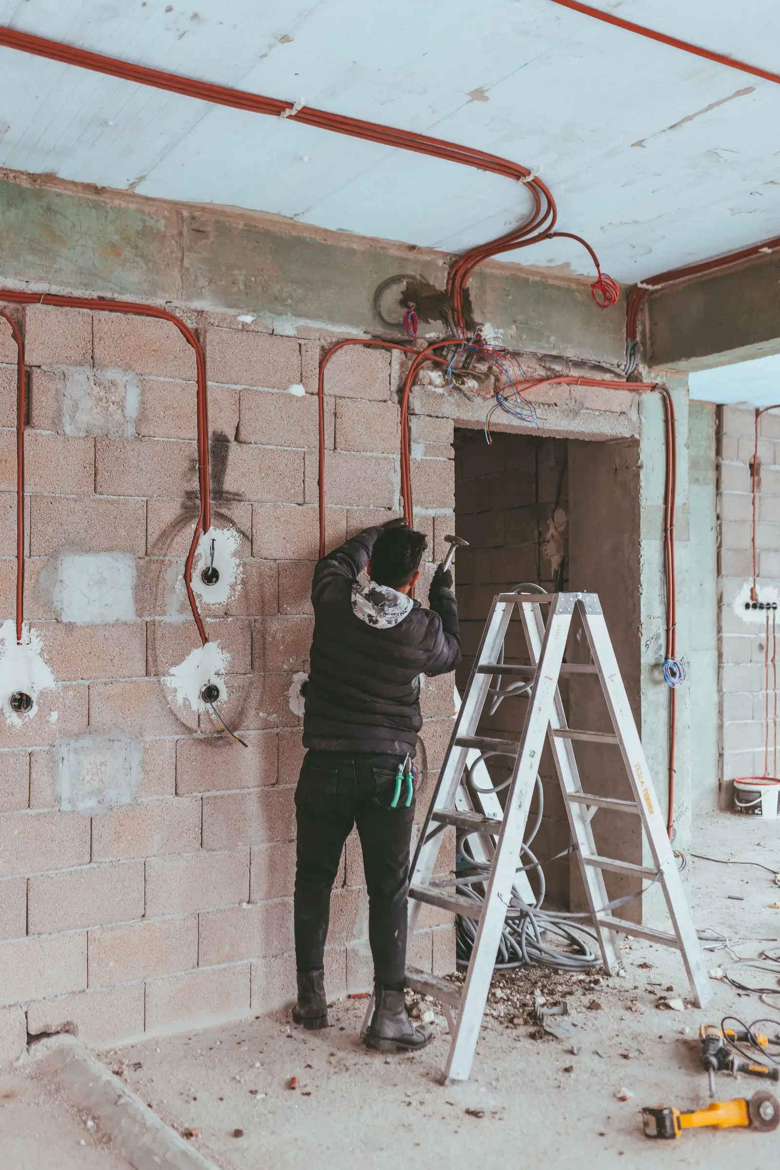 Worker beside a stepladder in a gutted room with new cable runs chased into the block walls