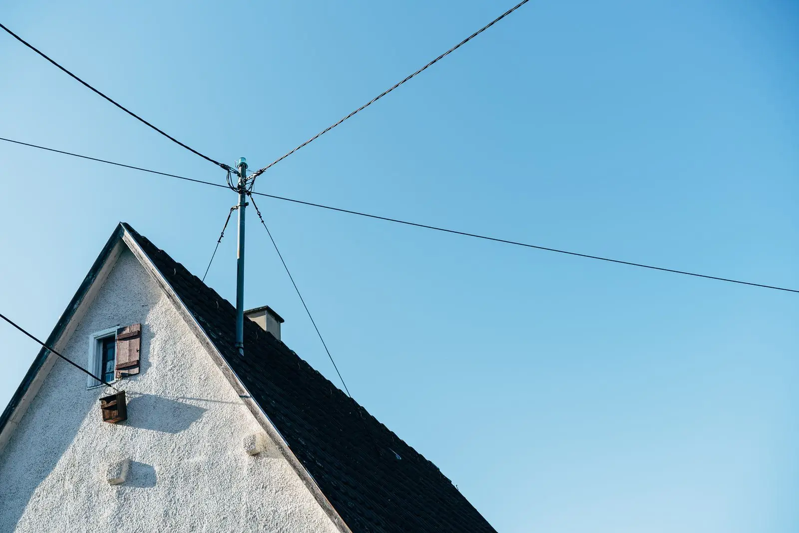 Overhead wires running to the gable end of a house under a blue sky