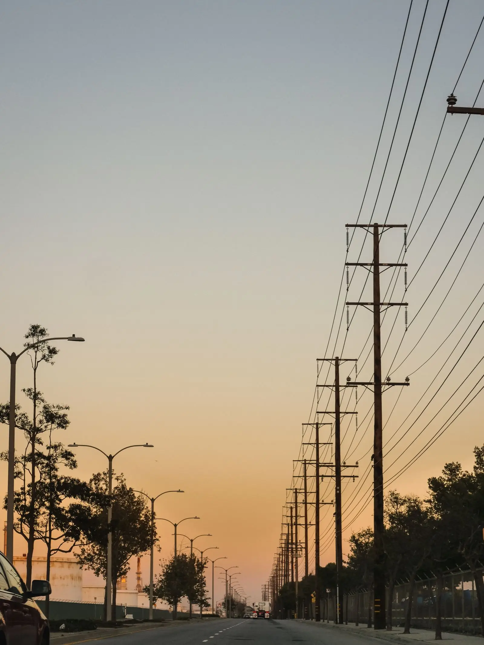 Row of utility poles and power lines against an orange evening sky